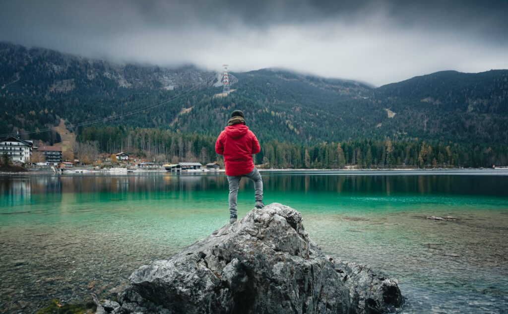 Person steht auf einem Felsen und genießt die Panoramaaussicht auf den Eibsee am Fuße der Zugspitze